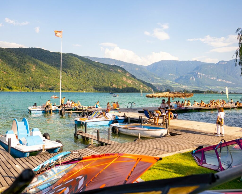 foto delle attività estive al lago di caldaro con persone che prendono il sole e pedalò